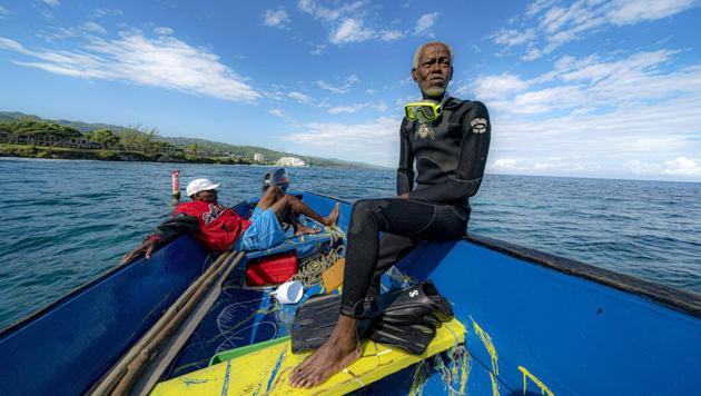 Everton Simpson (R), on a boat in-between dives on the White River Fish Sanctuary in Ocho Rios, Jamaica. Simpson steers the boat to an unmarked spot that he knows as the “coral nursery.” ‘’It’s like a forest under the sea,” he says, strapping on blue flippers and fastening his oxygen tank before tipping backward into the azure waters. (David J. Phillip / AP)