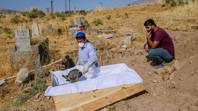 A worker holds the covered head of a corpse of a 15-year-old boy who died in 1997 in an accident in Hasankeyf as his 28-year-old brother Fatih (R) looks on, as they ready to transport it to the new cemetery. Fatih said, he remember the day his brother died, he was climbing on the leg of the historical bridge to catch some pigeons but fell and died, adding that “today I went back to his funeral again”. (Bulent Kilic / AFP)