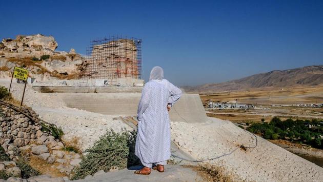 An elderly woman looks at the newly built stone wall near Hasankeyf. In the background is Hasankeyf’s ancient citadel, one of the few monuments high enough to survive the rising waters, but is now fronted by a huge, white stone wall to protect it. (Bulent Kilic / AFP)