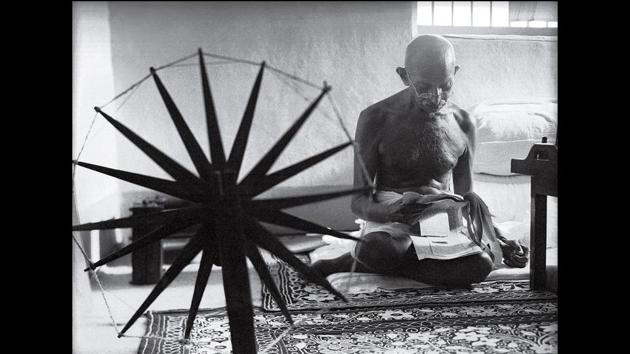 A 1964 photohraph of Gandhi taken by Margaret Bourke White shows him reading clippings with a charkha in the foreground.(Photo courtesy: National Gandhi museum)