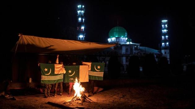 Men hold Azad (independent) Kashmir's and Pakistan's flag as they take a break from guard duty near Jinab Sahib in Anchar neighbourhood. “I am spending the night outdoors so I can protect my family and not let Indians, who have been committing atrocities on us, to enter,” said Fazil, a 16-year-old student. (Danish Siddiqui / REUTERS)