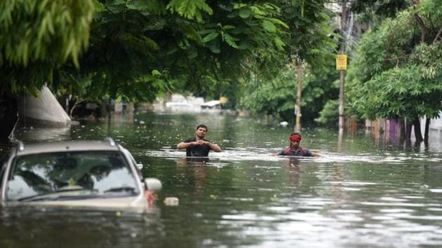 Commuters wade through waist-deep water as a car is partially submerged in Patna. The latest spell of rainfall is due to extended low pressure areas creating monsoon trough in different parts of the country, which would result in more showers in the next five days, according to the India Meteorological Department (IMD). (Parwaz Khan / HT Photo)