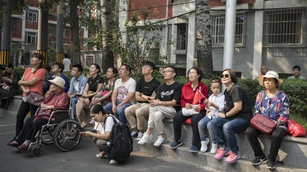 People sit on a wall watching a screen broadcasting the military parade for the 70th anniversary of the People's Republic of China in Beijing. The Communist Party has repeatedly defied the odds to remain in power for seven decades. Under Mao, tens of millions of people died during the disastrous Great Leap Forward, and the country was plunged into violent chaos during the decade-long Cultural Revolution. (Giulia Marchi / Bloomberg)