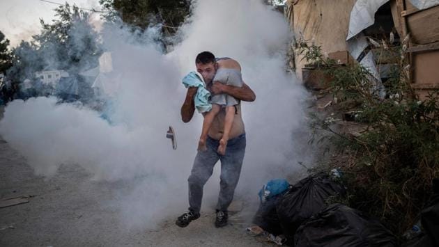 A man holds a boy during clashes with police outside the refugee camp of Moria on the Greek island of Lesbos. At least one migrant died on September 29, 2019, after a fire broke out in Moria, the over-crowded refugee camp on the Greek island of Lesbos, Greece's Health Ministry said. (Angelos Tzortzinis / AFP)