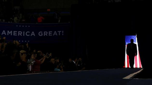 US President Donald Trump is silhouetted against a US flag as he holds a campaign rally in Lake Charles, Louisiana. (Leah Millis / REUTERS)