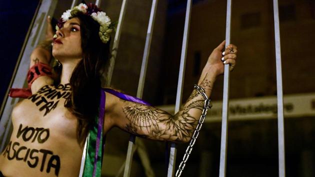 An activist of women's rights organisation Femen, is chained to the gate of Palacio Vistalegre, with the words "against fascist vote" painted on her body during a protest against a campaign rally of Spanish far-right party VOX, in Madrid, Spain. (Oscar Del Pozo / AFP)