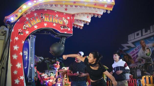 A girl hits a boxing power punch machine at the fair. Music and flashing lights strike visitors on arrival at the fairground, which is constantly engulfed in smoke from the food grills and an endless mix of food flavours. (Andreea Alexandru / AP)