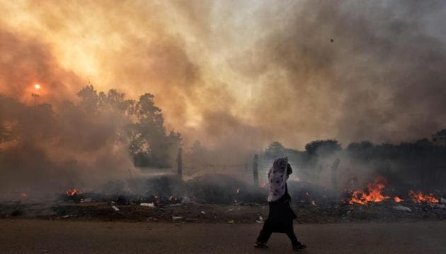 A lady passes through a row of garbage that caught fire at Sonia Vihar in New Delhi.(Photo:Sanchit Khanna?HT photo)