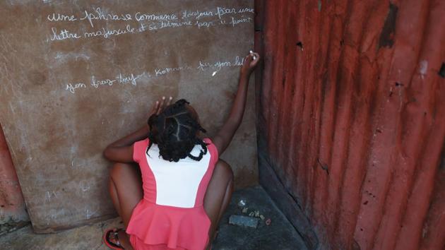 A girl writes in French and Creole on a chalkboard: “A sentence always begins with a capital letter and ends with a period,” outside a one-room home in the Cite Soleil district of Port-au-Prince. Residents of Cite Soleil say access to basic services, jobs, and security has been declining and many are participating in the protests. Schools have been closed for weeks due to the protests. (Rebecca Blackwell / AP)