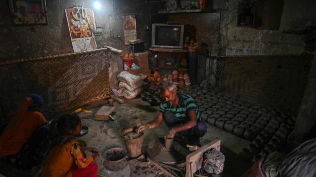 A potter makes clay pots as his family looks on at their residence at Kumhar Gram. Potter Dinesh Kumar, like many others in the village, learnt about clay from his father and is now passing on the skills to his young children. (Money Sharma / AFP)
