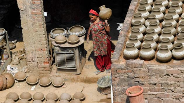 A woman carries an earthen pot inside her residence, with others in various stages of completion arranged all over. One of Jagmohan’s brothers carves designs on them, then the women of the family take the finished works to the roof, where they are left to dry under the sun. Once dry, they are placed in a rooftop wood oven to bake. (Money Sharma / AFP)