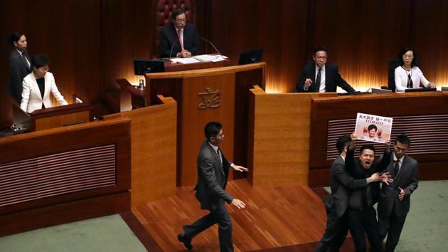 Security officers surround pro-democracy lawmaker Gary Fan, (2nd R, front), as Hong Kong Chief Executive Carrie Lam, (top, left), delivers her speech at a question and answer session with lawmakers at the Legislative Council in Hong Kong. (Mark Schiefelbein / AP)