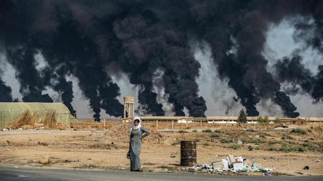 A woman stands along the side of a road on the outskirts of the town of Tal Tamr near the Syrian Kurdish town of Ras al-Ain along the border with Turkey in the northeastern Hassakeh province, with the smoke plumes of tire fires billowing in the background to decrease visibility for Turkish warplanes that are part of operation “Peace Spring”. (Delil Souleiman / AFP)