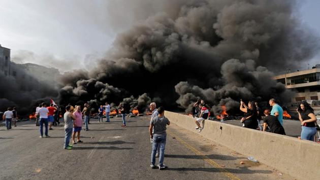 Lebanese demonstrators gather on a highway blocked by a tire fire during a protest in Nahr Ibrahim, north of Beirut. “We came to the streets because we can no longer bear this situation. This regime is totally corrupt,” said Fadi Issa, 51, who was marching with his son. “They are all thieves, they come to the government to fill their pockets, not to serve the country. (Joseph Eid / AFP)