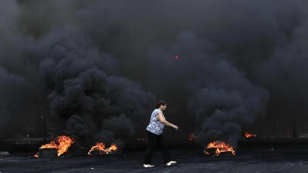 A woman walks by burning tires that were set fire to block a road during the protest. The demonstrations follow warnings by economists, investors and rating agencies that indebted Lebanon’s economy and graft-entrenched financial system are closer to the brink than at any time since the war-torn 1980s. (Hassan Ammar / AP)