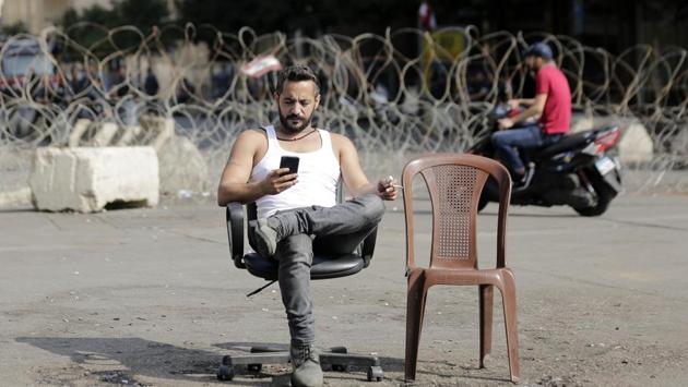 An anti-government protester checks his phone after spending Sunday night protesting in front of the government palace in Beirut. Following Hariri’s speech at the presidential palace, thousands of people gathered outside his office in downtown Beirut chanting: “The people want to bring down the regime,” and “Revolution, revolution!” (Hassan Ammar / AP)