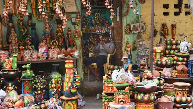 A shopkeeper engaged on his mobile phone as finished products await buyers. Ved Prakash Prajapati, another resident, said it was wrong to call the potters as “polluters” for following traditional methods of pottery. “Almost 40% of the families here have already given up pottery, and if our kilns are shut down, we will be forced to move back to our native village in Rajasthan,” said Ved Prakash. (Vipin Kumar / HT Photo) 