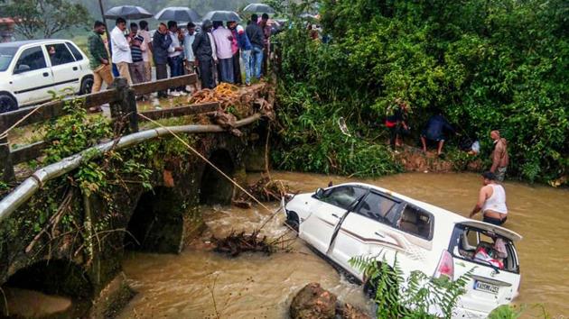 Onlookers watch after a car slid from a bridge to a stream near Chikmagalur on Friday. Parts of Karnataka have faced a deluge for second time in two months and the toll since last week rose to 13. The second spell of downpour since October 18 damaged around 10,000 houses and rendering over 7,000 people homeless in 16 districts, including Belagavi in north Karnataka which bore the brunt of the flood fury in August. (PTI)