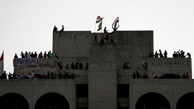 The scene at Tahrir was chaotic, with some protesters climbing atop multistorey business centres to wave Iraqi flags and others torching tyres in rubbish-littered streets. (Thaier Al-Sudani / REUTERS)