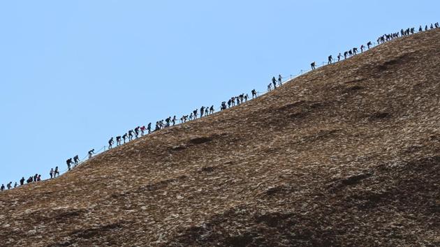 Tourists climb Uluru on Friday, the last day people were able to climb here. The ceremony was held two days after a final surge of tourists who had flocked to central Australia scaled the giant red monolith before its closure to climbers. (Lukas Coch / AAP via REUTERS)