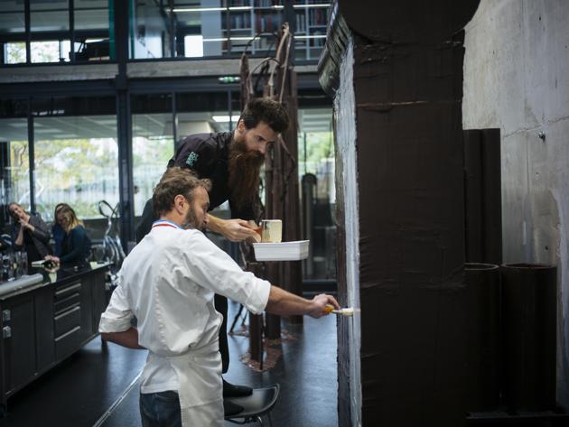 French chocolate maker Patrick Roger, front and his creative assistant Angelo Dao add white chocolate to a dark chocolate reproduction of the Berlin wall, in Sceaux, outside Paris, Wednesday, Oct. 30, 2019 to mark the upcoming 30th anniversary of the fall of the Berlin Wall. The chocolate wall will be destroyed on Nov.9. (AP Photo/Kamil Zihnioglu) (AP)
