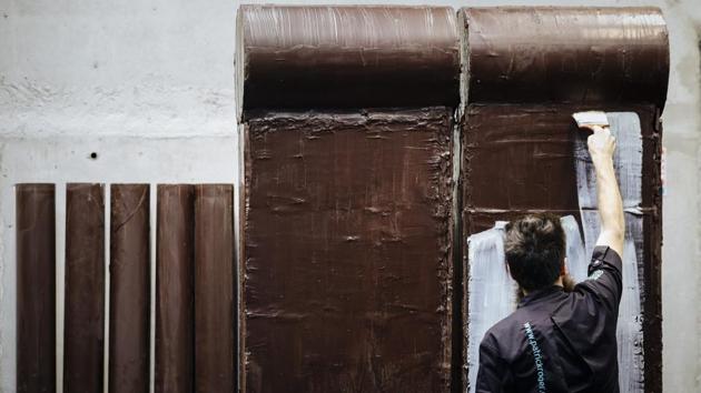 French chocolate maker Patrick Roger's creative assistant Angelo Dao adds white chocolate to a dark chocolate reproduction of the Berlin wall, in Sceaux, outside Paris, Wednesday, Oct. 30, 2019 to mark the upcoming 30th anniversary of the fall of the Berlin Wall. The chocolate wall will be destroyed on Nov.9. (AP Photo/Kamil Zihnioglu) (AP)