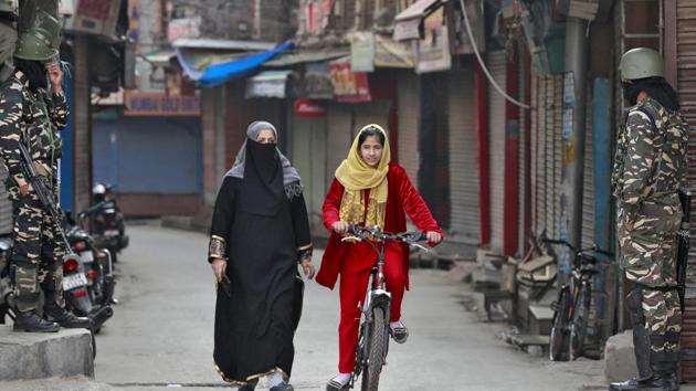 A Kashmir girl rides her bike past a security force personnel standing guard in front closed shops in a street in Srinagar.(REUTERS) A Kashmir girl rides her bike past a security force personnel standing guard in front closed shops in a street in Srinagar.(REUTERS)