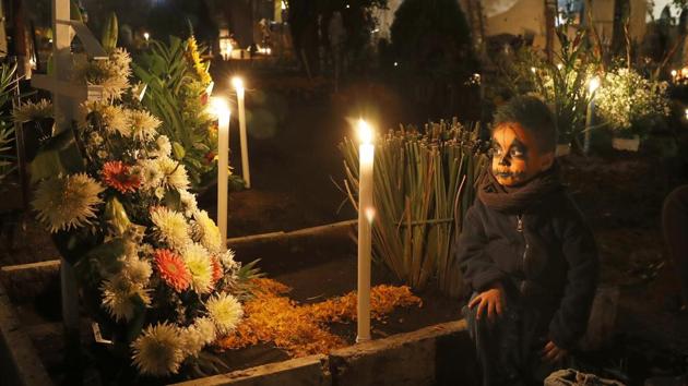 A child sits next to a tomb, illuminated with candles in the San Gregorio Atlapulco cemetery. (AP) 
