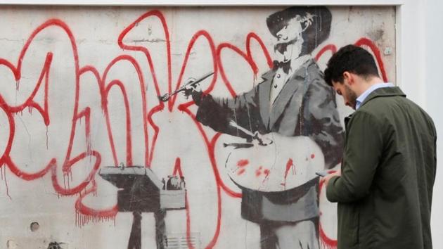 A man checks his phone near a Banksy mural known as The Painter, which first appeared in 2008, before it is officially unveiled in Notting Hill, London, Britain. (REUTERS) A man checks his phone near a Banksy mural known as The Painter, which first appeared in 2008, before it is officially unveiled in Notting Hill, London, Britain. (REUTERS)