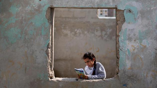 A Palestinian UNRWA schoolgirl holds her book as she stands by a window outside her family home in Al-Shati refugee camp in Gaza City. (Mohammed Salem / REUTERS)