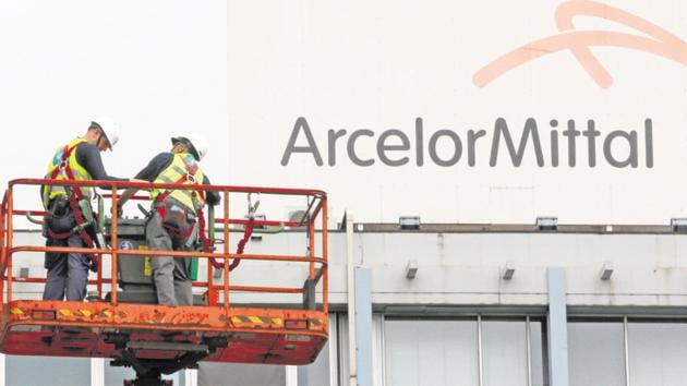Workers stand near the logo of ArcelorMittal at the steel plant in Ghent, Belgium.(Reuters File)