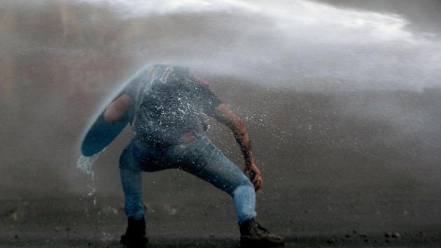 A demonstrator leans to elude the riot police water cannon during a protest against the government in Santiago, Chile. President Sebastian Pinera condemned on Sunday for the first time what he called abuses committed by police in dealing with four weeks of violent unrest that have rocked Chile and left 22 people dead and more than 2,000 injured. (CLAUDIO REYES / AFP) A demonstrator leans to elude the riot police water cannon during a protest against the government in Santiago, Chile. President Sebastian Pinera condemned on Sunday for the first time what he called abuses committed by police in dealing with four weeks of violent unrest that have rocked Chile and left 22 people dead and more than 2,000 injured. (CLAUDIO REYES / AFP)