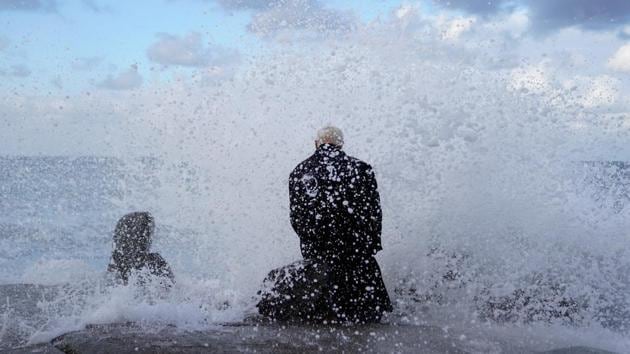 Dressed in a long wool trench coat Bruce Parker sits on a rock enjoying the waves spraying him as they crash on the beach during the arrival of a winter storm in Oceanside, California, US. (Mike Blake / REUTERS)