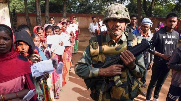 A paramilitary trooper keeps vigil as people wait in queues to cast their votes at a polling station during the first phase of Jharkhand Assembly elections in Maoist-affected Latehar district on Saturday.(PTI)