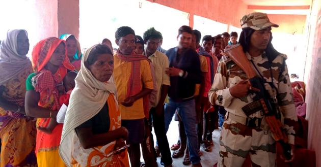 ITBP personnel stands guard outside the polling booth as people stand in a queue to cast their vote during the first phase of Jharkhand assembly elections, in Latehar on Saturday.(ANI Photo)