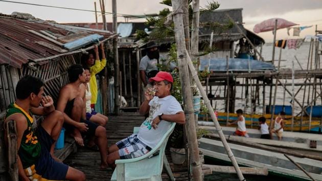Residents socialise outside of their bamboo huts. Solar panels are installed on many rooftops for electricity, mostly to watch television that’s shared between neighbours. On days that power is low, residents pass the time by gambling. (Eloisa Lopez / REUTERS)