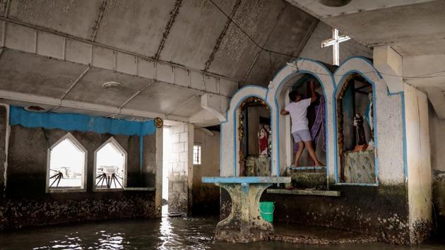 A church caretaker cleans a crucifix in the church at Sitio Pariahan. Danica remembers their village wasn’t always like this. She recalls basketball tournaments and grand feasts so popular that visitors from nearby towns would flock to watch performances, and celebrate mass at the church. The court is now fully submerged, and the church once filled with devotees is stained with moss. (Eloisa Lopez / REUTERS)