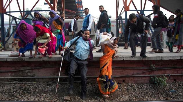 Vinod Kumar Sharma (L) walks from a platform onto the rail tracks with his wife Indrapti (R) after arriving at Okhla railway station in New Delhi. Sharma told AFP that people always help him to get on and off trains. “The people are good. But there are broken roads and open sewage holes which are always a risk,” he added. (Xavier Galiana / AFP)