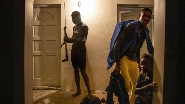 Nicholas Bingham (L), grabs his speargun while leaving to go spearfishing. Bingham and Delroy Gooden put on their flippers, masks and snorkels, then wrapped their faces to protect against stinging jellyfish. But that’s not the only threat lurking in the water: In addition to sharks, wardens are patrolling, scouting for illegal fishing in protected fish sanctuaries. (David Goldman / AP)