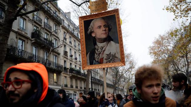 A woman holds a portrait of French President Emmanuel Macron painted as a royalty with a sign on top of it reading "14 May 2017 restoration of the monarchy" during a rally against the pension overhauls, in Paris. France scrambled to make contingency plans for a huge strike against pension overhauls that poses one of the biggest challenges yet to French President's sweeping reform drive. (Thomas Samson / AFP)