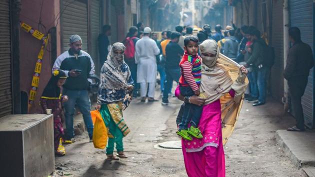 A woman carries a child as she walks past the spot where fire broke out in a factory in New Delhi on Sunday.(PTI Photo)