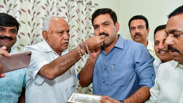 Karnataka Chief Minister BS Yediyurappa offers sweets to his younger son BY Vijayendra after BJP won in 12 out of 15 assembly constituencies in the bypolls in Karnataka.(PTI)