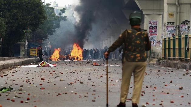 A policeman stands guard as protesters burn public property at Seelampur in Northeast Delhi on Tuesday during a protest against the amended citizenship law.(Sanchit Khanna/HT PHOTO)