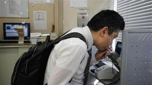 Norihito Arima, blows into a breathalyzer before picking up his key at the company’s Akabane office. The daily muster wraps up as drivers — 95% are men — bow toward a small Shinto shrine. And for good measure, they undergo a breathalyzer before hitting the road. (Jae C. Hong / AP) 