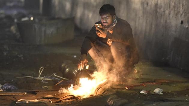 A man sits near a bonfire to warm himself on a cold winter evening, at Connaught Place, in New Delhi, India.(Sonu Mehta/HT file photo)
