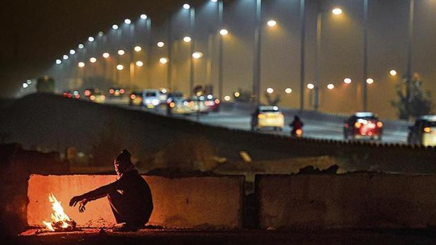 A man warms himself by a bonfire as cars ply in the background on a cold and wintry night, in New Delhi.(PTI Photo)