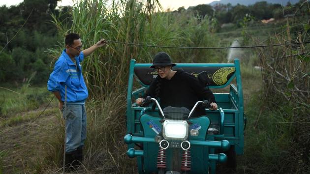 Da Wang holds up a wire for Xing Zhen as he drives a vehicle through his farm at AnotherCommunity. “Whatever they do, I just hope they make something of it,” said the village’s Communist Party chief, surnamed Lin to Reuters. (Tingshu Wang / REUTERS)
