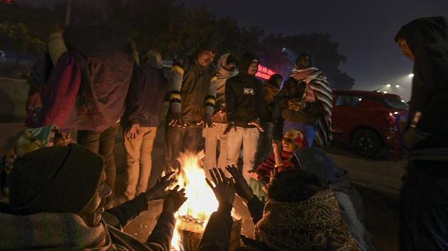 People sit beside a fire to keep themselves warm on a cold winter evening outside AIIMS in New Delhi on Monday.(PTI Photo)