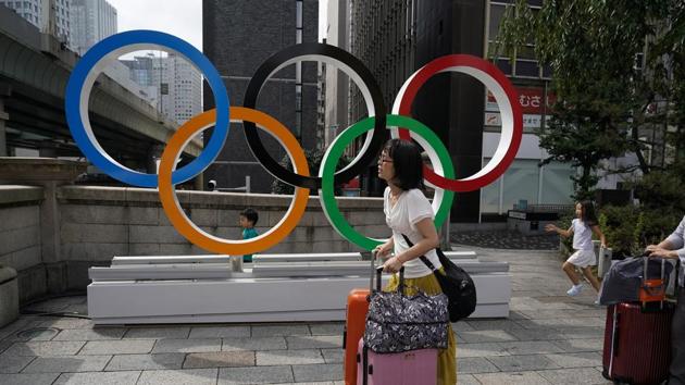 In this file photo, tourists walk with their luggage past the Olympic rings in Tokyo.(AP) In this file photo, tourists walk with their luggage past the Olympic rings in Tokyo.(AP)