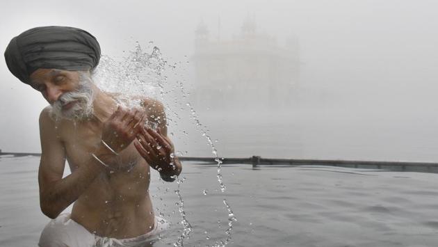 A devotee takes a dip in a sarovar amid dense fog on a cold morning at the Golden Temple in Amritsar, Punjab. (Sameer Sehgal / HT Photo)